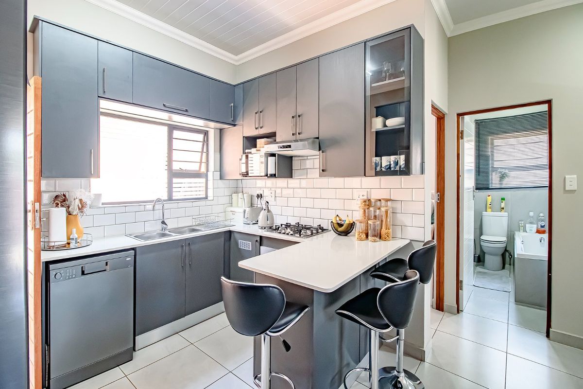 Modern kitchen featuring dark grey cabinetry, white quartz countertops, subway tile backsplash, gas hob, and integrated dishwasher, with an adjacent bathroom visible.