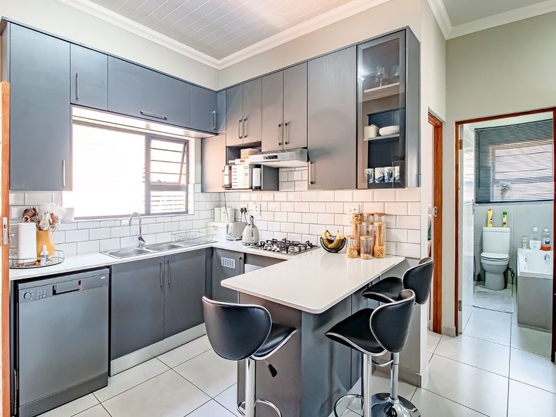 Modern kitchen featuring dark grey cabinetry, white quartz countertops, subway tile backsplash, gas hob, and integrated dishwasher, with an adjacent bathroom visible.