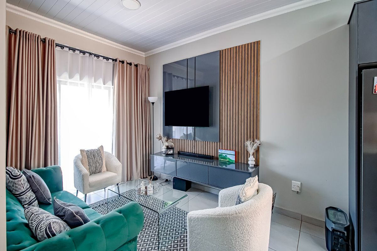 A well-maintained living room featuring a modern media wall with slatted wood accents, tiled flooring, and a tongue and groove ceiling.