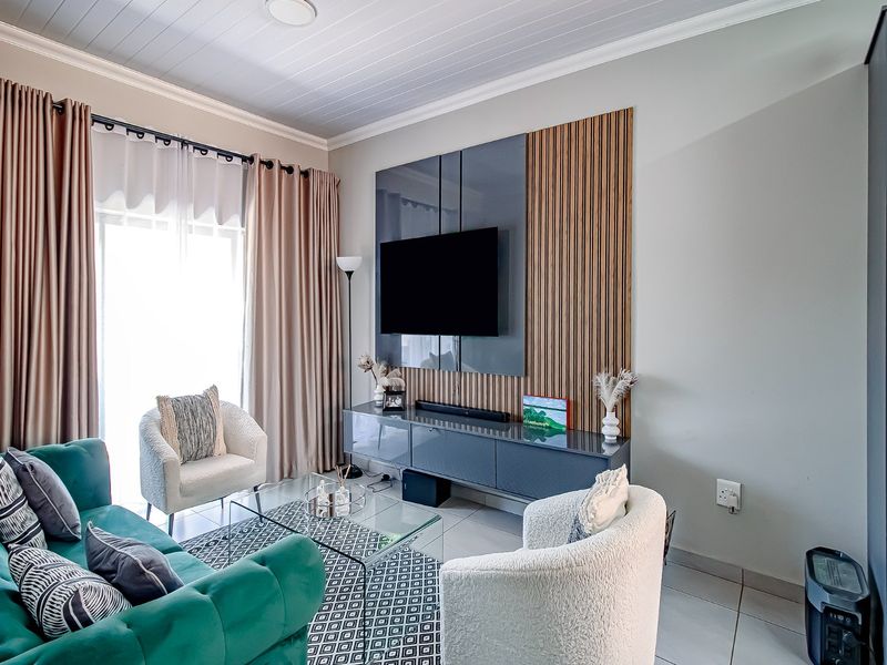 A well-maintained living room featuring a modern media wall with slatted wood accents, tiled flooring, and a tongue and groove ceiling.