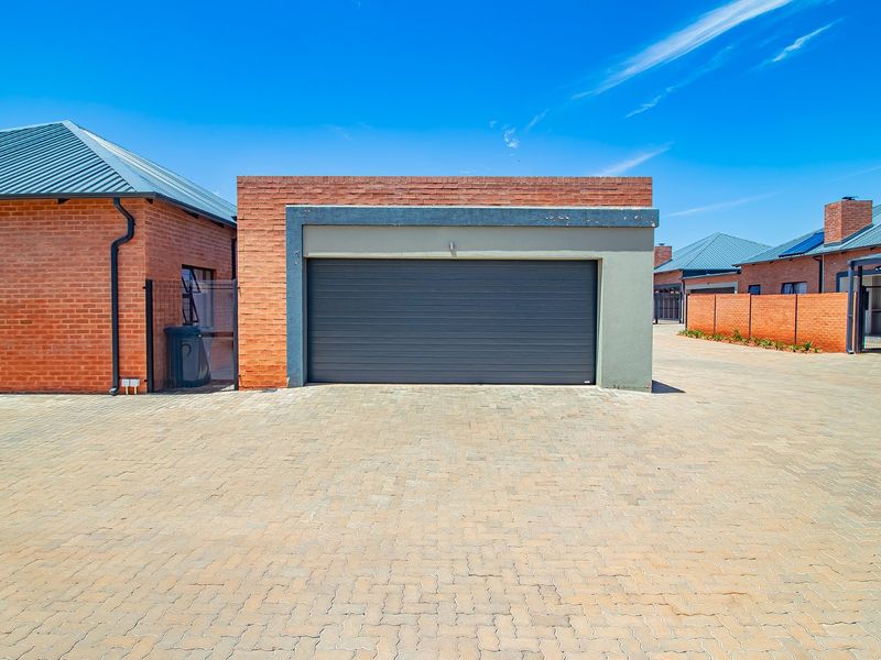 A modern townhouse garage featuring a brick facade and a dark sectional garage door, situated on a paved driveway.