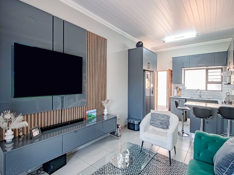 Modern open-plan living area featuring a sleek built-in media wall with timber accents, flowing into a contemporary kitchen with grey cabinetry and tiled floors.