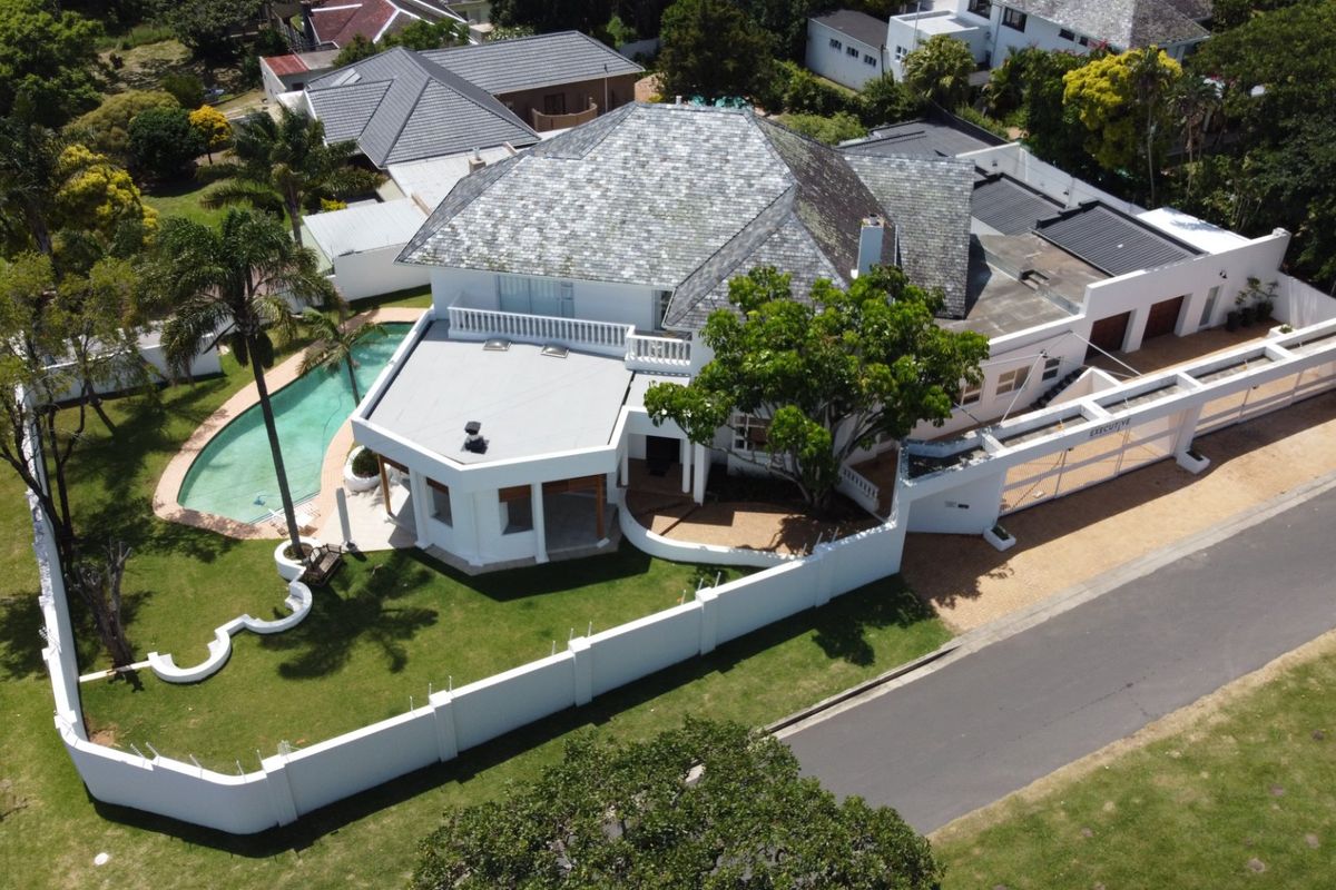Aerial view of a large residential property featuring a swimming pool, expansive garden, perimeter wall, and multiple garage bays.
