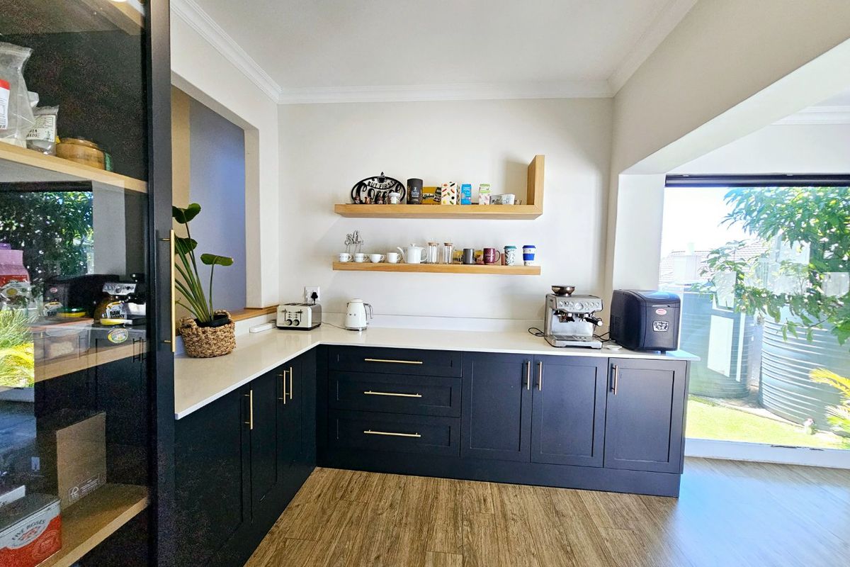 A modern kitchen area featuring dark cabinetry, light stone countertops, and floating timber shelving, with direct access to the outdoor garden area.