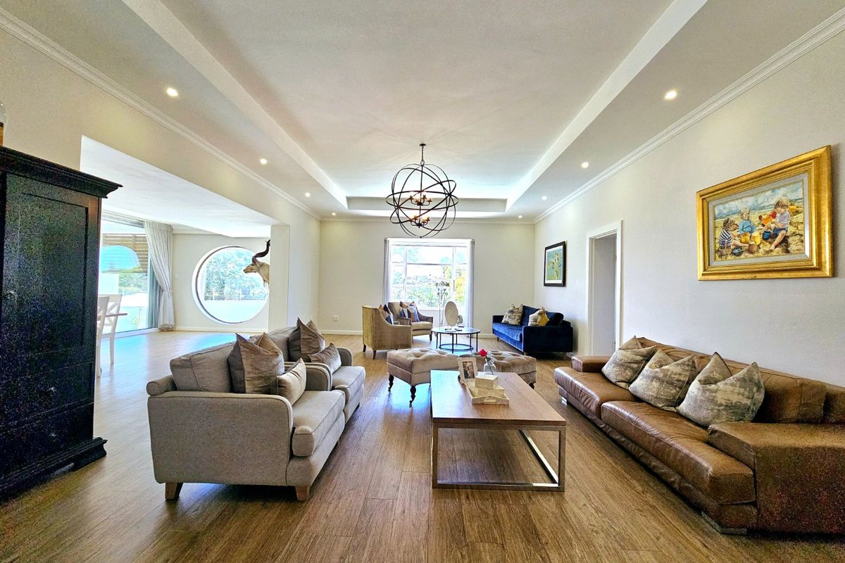 Spacious living room featuring a recessed ceiling with cove lighting, wood-look tile flooring, and a distinctive circular window providing natural light.