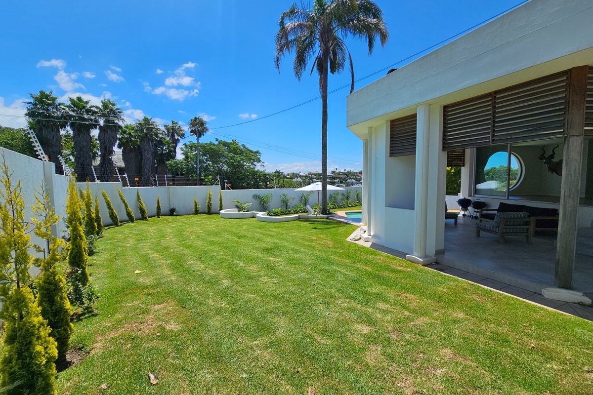 A well-maintained rear garden featuring a manicured lawn, perimeter wall with electric fencing, and a covered patio area overlooking a swimming pool.