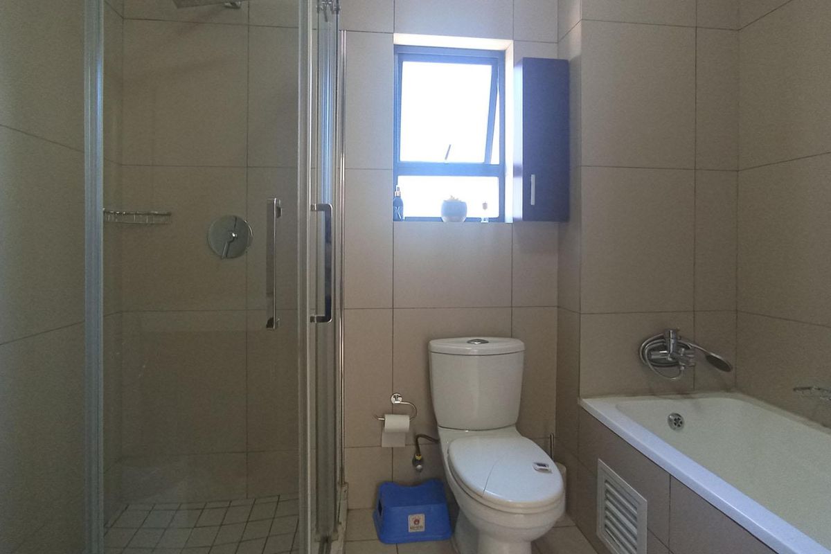 A functional bathroom featuring a glass-enclosed shower, a standard bathtub, and a toilet with neutral wall tiling.