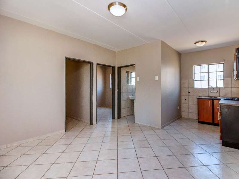 An open-plan living and kitchen area featuring tiled flooring, built-in cabinetry, and neutral wall tones, offering a versatile space for customization.