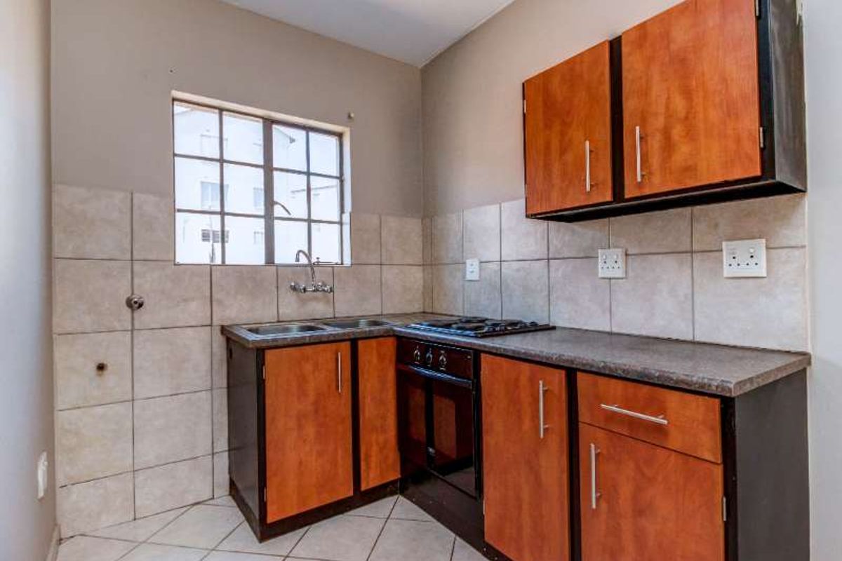 A functional kitchen featuring built-in wooden cabinetry, laminate countertops, a gas hob, an integrated oven, and tiled finishes throughout.