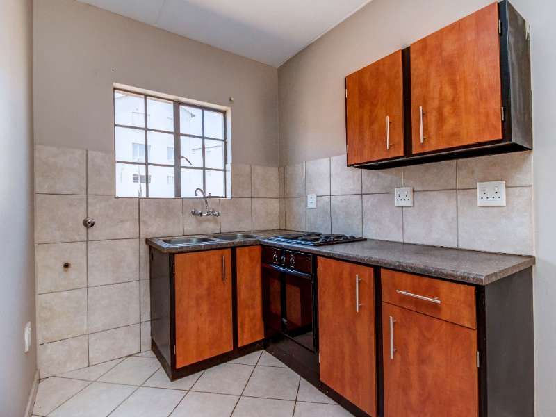 A functional kitchen featuring built-in wooden cabinetry, laminate countertops, a gas hob, an integrated oven, and tiled finishes throughout.