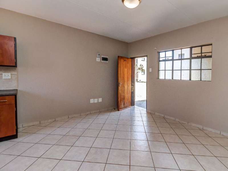 An empty open-plan living and kitchen area featuring tiled flooring, a wooden exterior door, and a grid-style window.
