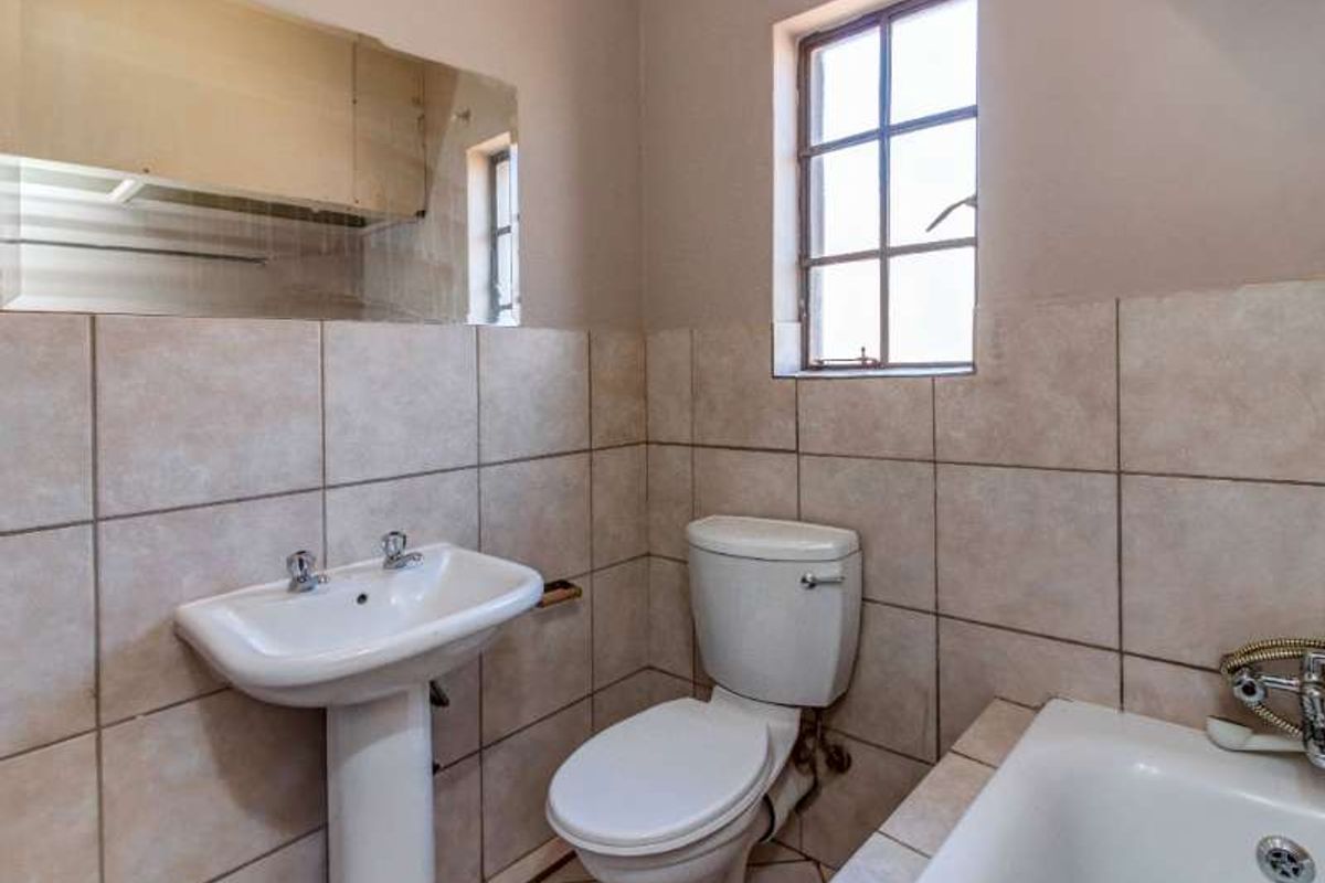 A functional bathroom featuring a pedestal basin, toilet, and bathtub with tiled walls and flooring, offering a clean, neutral space ready for updates.