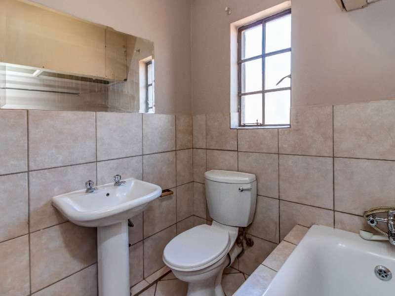 A functional bathroom featuring a pedestal basin, toilet, and bathtub with tiled walls and flooring, offering a clean, neutral space ready for updates.
