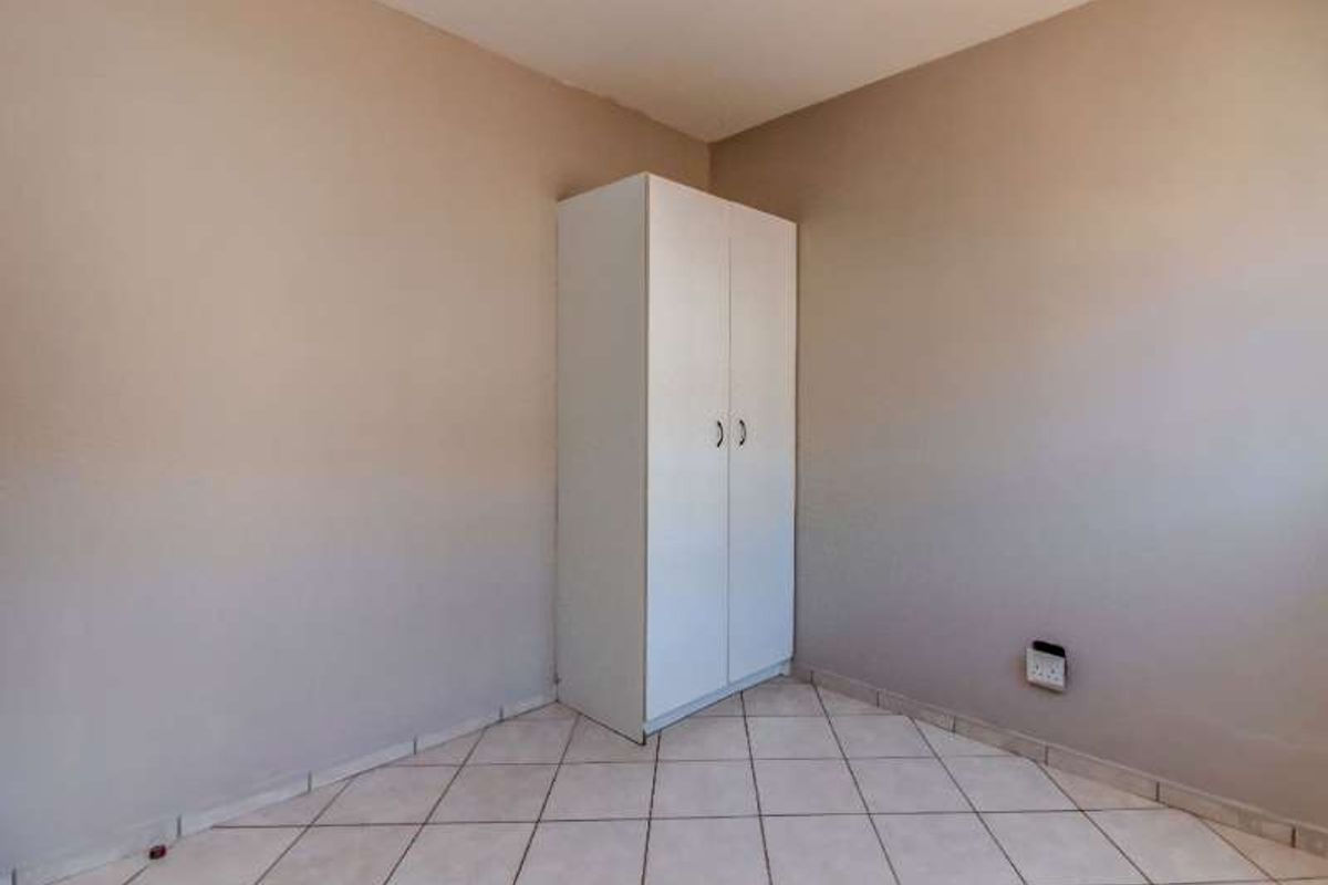 A simple, empty bedroom featuring neutral wall paint, tiled flooring, and a built-in white wardrobe.