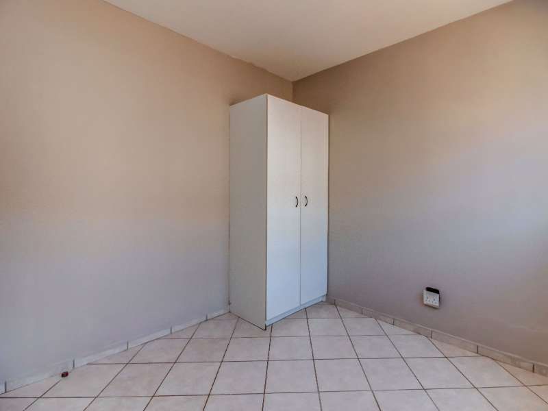 A simple, empty bedroom featuring neutral wall paint, tiled flooring, and a built-in white wardrobe.