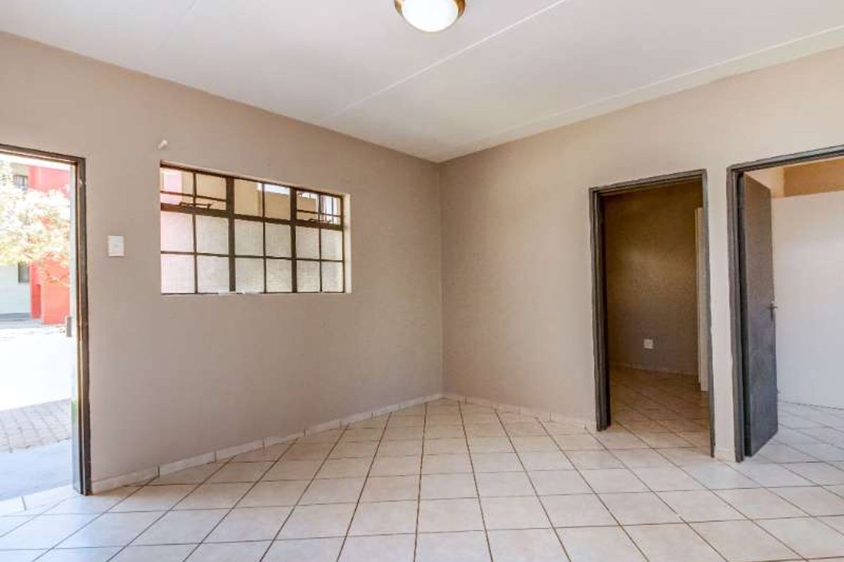 An empty living room featuring neutral wall paint, tiled flooring, and natural light through a metal-framed window.