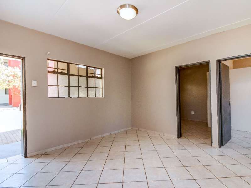 An empty living room featuring neutral wall paint, tiled flooring, and natural light through a metal-framed window.