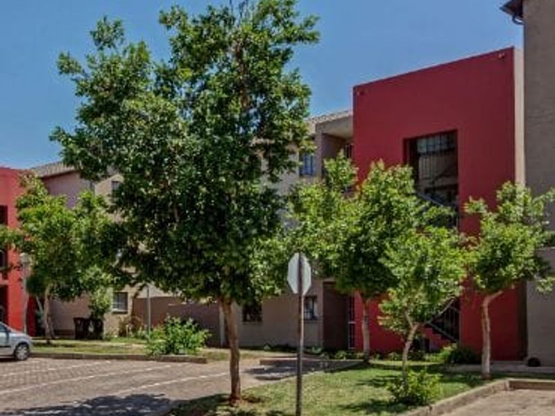 Exterior view of an apartment complex featuring paved parking areas, landscaped garden beds, and modern red and neutral facade finishes.