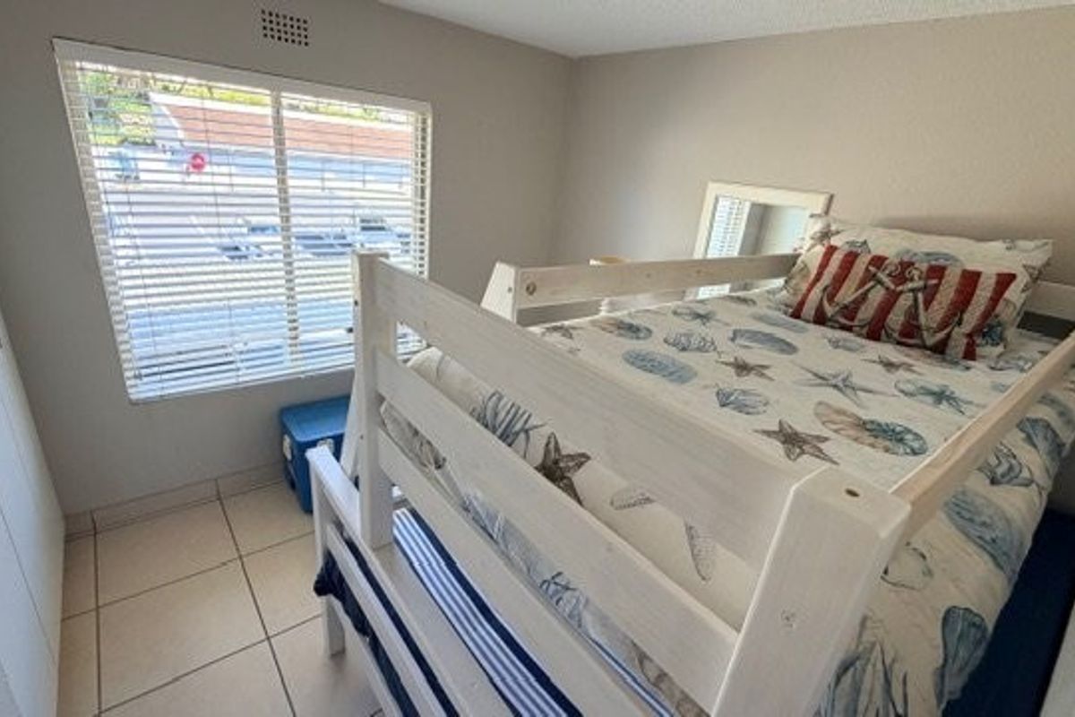 A functional bedroom featuring built-in cupboards, tiled flooring, and a window with venetian blinds, providing a clean and practical living space.
