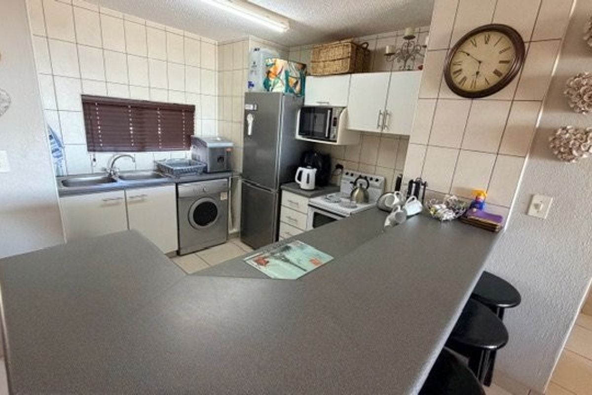Compact kitchen featuring tiled backsplash, laminate countertops, built-in cabinetry, and integrated appliances, including a breakfast bar area.