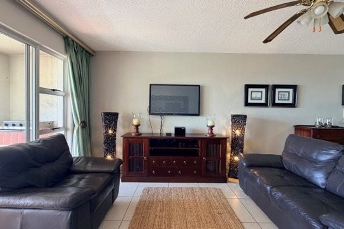 A comfortable living room featuring tiled flooring, a ceiling fan, and large sliding glass doors providing access to an outdoor patio area.