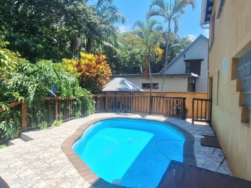 Outdoor pool area featuring a swimming pool with tiled surround, timber balustrades, and lush garden surroundings.
