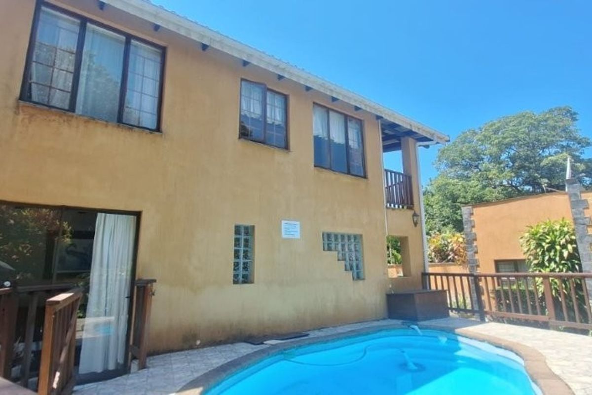 Rear exterior view of the house featuring a swimming pool, timber decking, and a stucco facade with glass block accents.