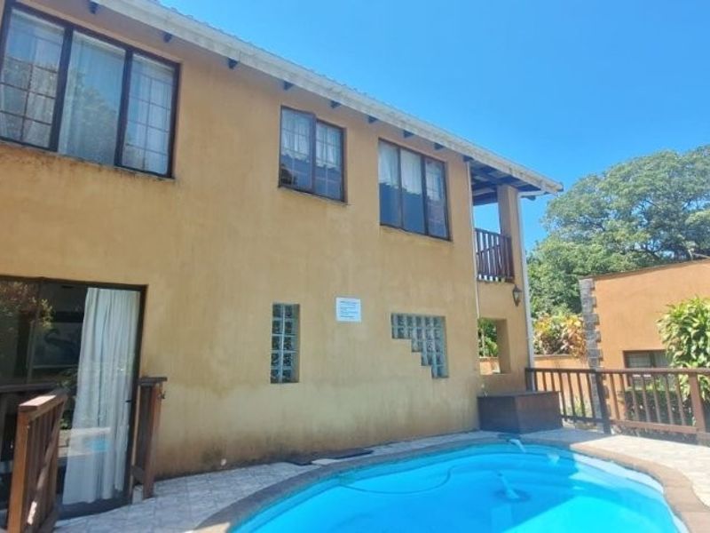 Rear exterior view of the house featuring a swimming pool, timber decking, and a stucco facade with glass block accents.