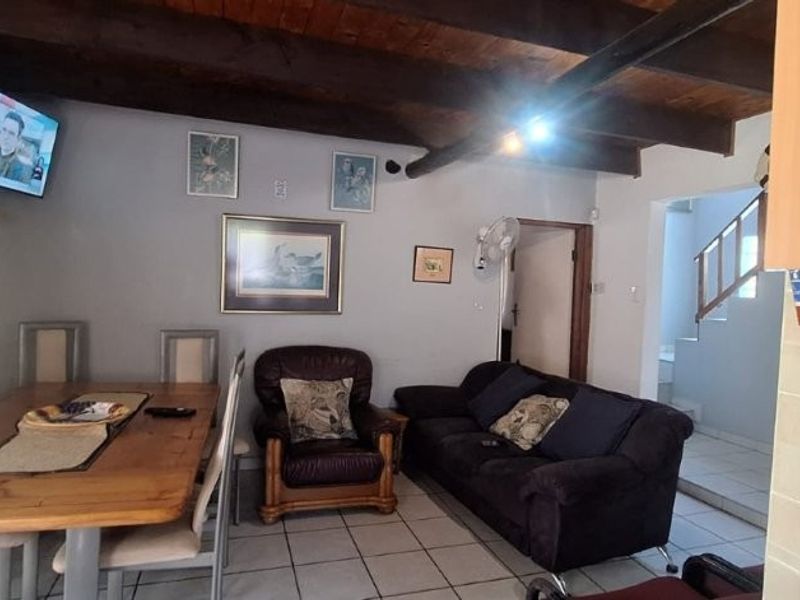 Open plan living and dining area featuring exposed timber ceiling beams and ceramic floor tiles, with an adjacent staircase leading to the upper level.