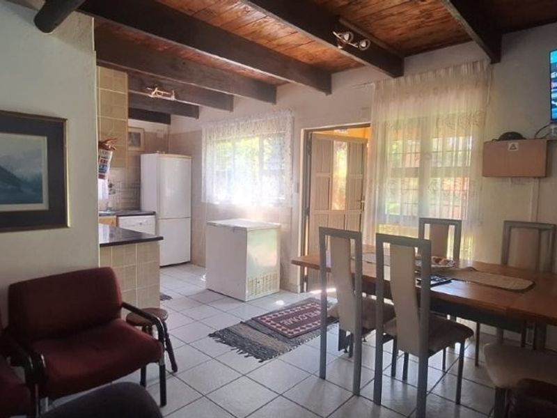 Open-plan living and dining area featuring exposed timber ceiling beams, tiled flooring, and an integrated kitchen space with functional cabinetry.