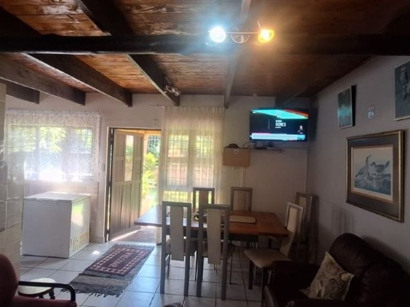 Open plan living and dining area featuring exposed timber ceiling beams, tiled flooring, and direct access to the outdoor space through a sliding door.