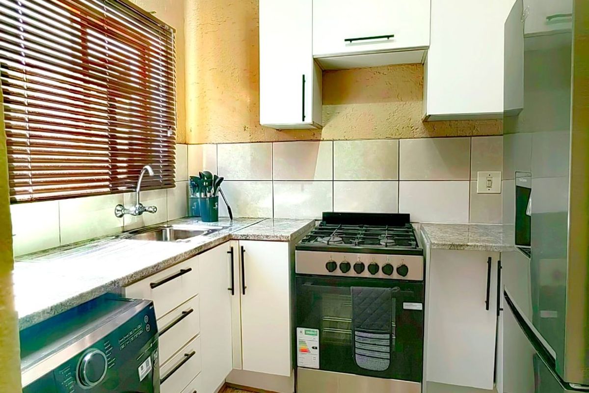 Compact kitchen featuring white cabinetry, granite countertops, tiled backsplash, and a gas stove, with wood-look flooring and venetian blinds.