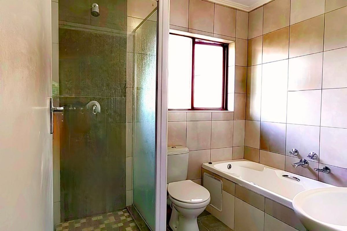 A functional bathroom featuring a separate shower enclosure, built-in bathtub, pedestal basin, and toilet, finished with neutral wall and floor tiling.