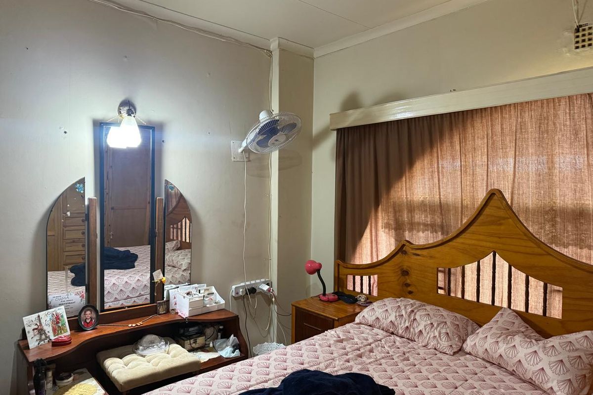 A bedroom featuring a wooden headboard, wall-mounted lighting, and a wall-mounted fan, requiring cosmetic updates to improve the overall aesthetic.
