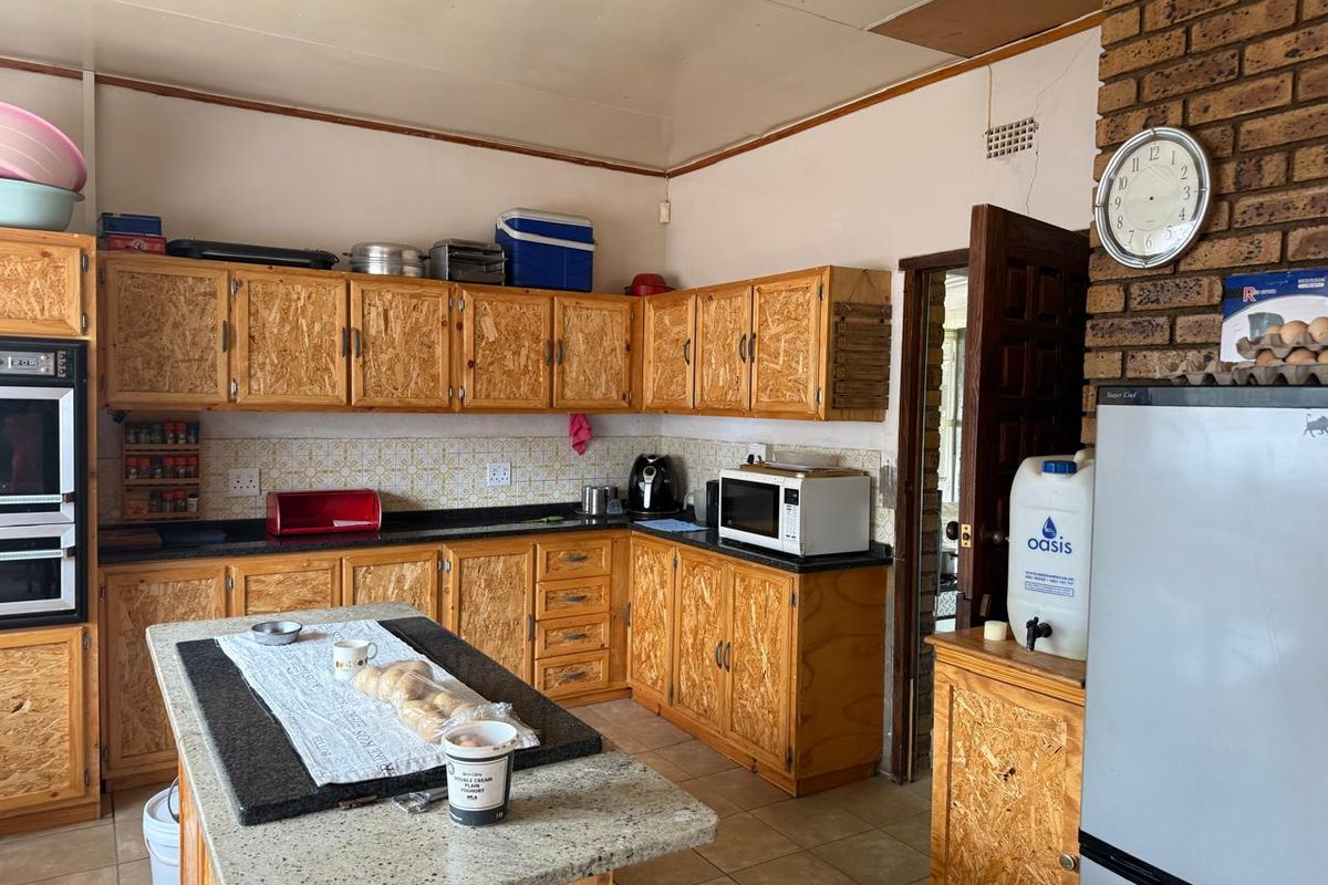 A dated kitchen featuring wooden cabinetry, granite countertops, and a brick feature wall, requiring cosmetic updates to modernize the space.