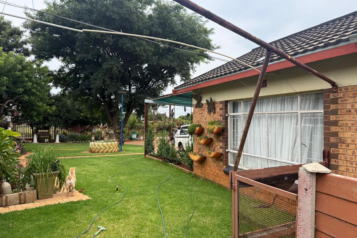 Rear view of the house featuring a brick facade, tiled roof, and a spacious garden area with a metal support structure.