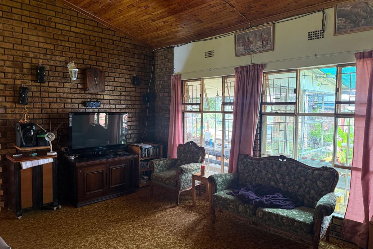 Spacious living room featuring exposed brick walls, a high timber ceiling, and large windows with security bars, offering a dated but character-filled interior space.
