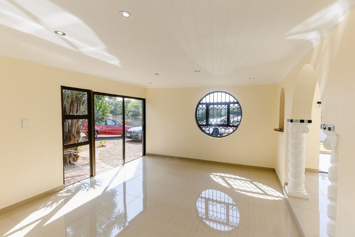 A bright, empty living area featuring polished tile floors, a unique circular window with security bars, and an elegant decorative column leading to an archway.