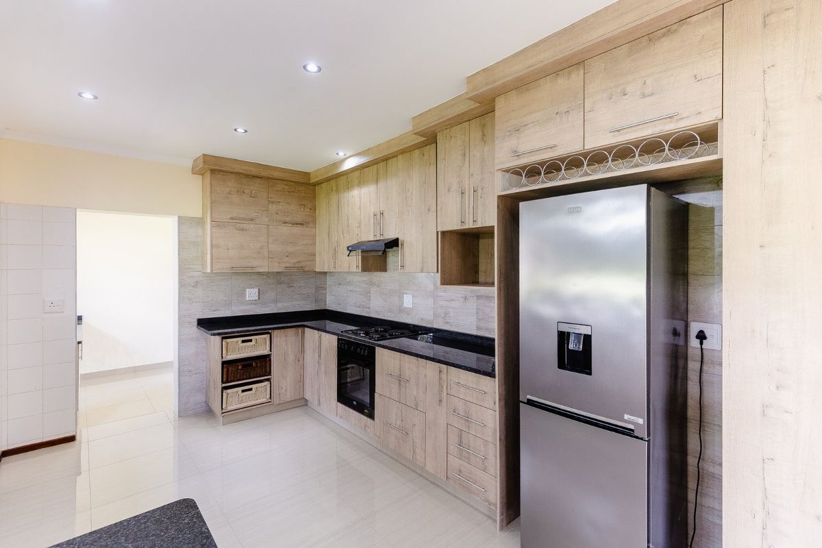 Modern kitchen featuring light wood-grain cabinetry, dark stone countertops, built-in oven, gas hob, and sleek tiled finishes throughout.