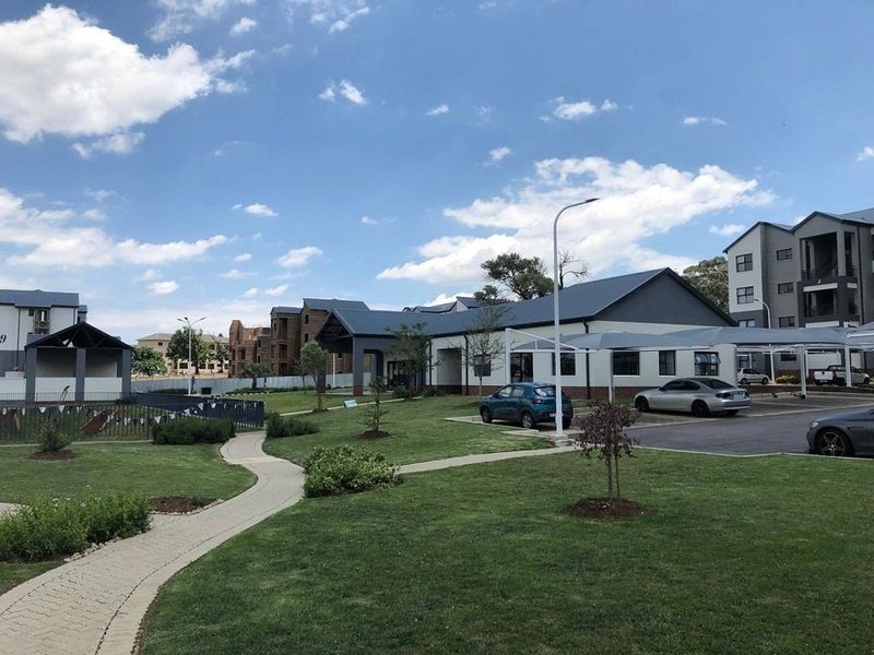 A view of the apartment complex grounds featuring landscaped lawns, paved walkways, and covered parking facilities under a clear blue sky.