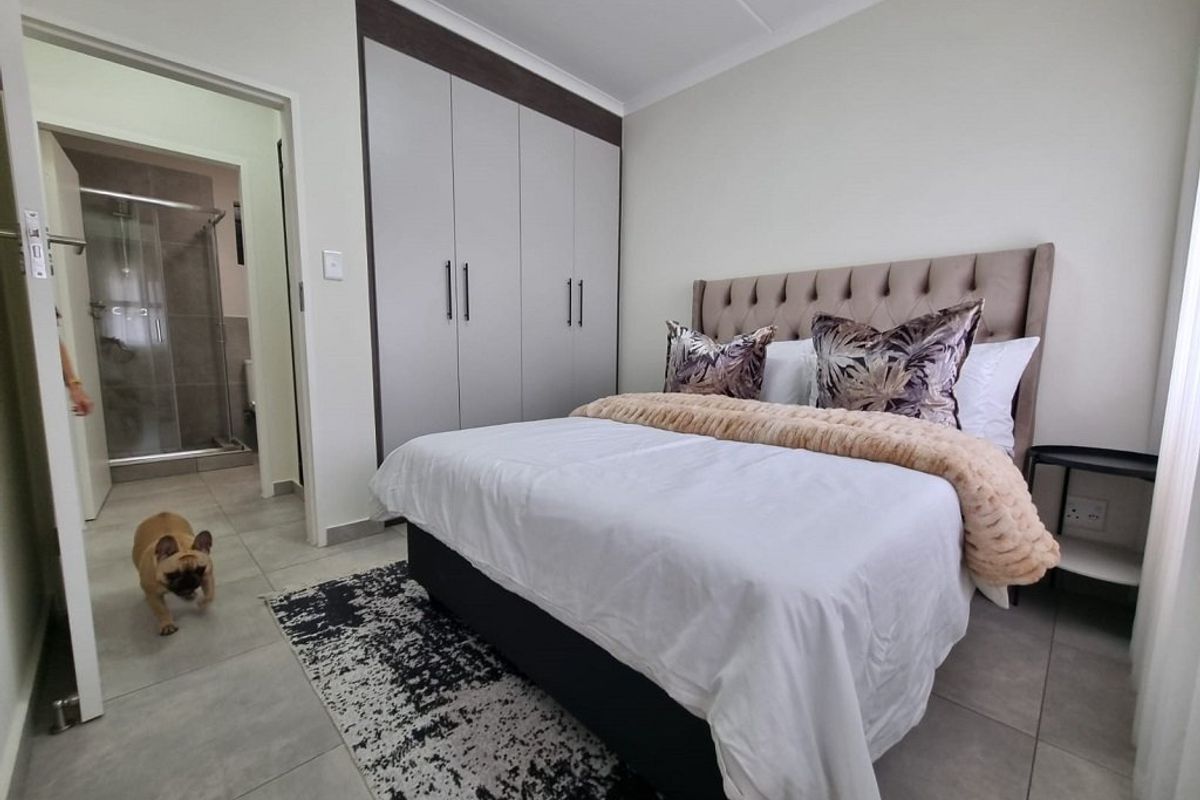 A well-maintained bedroom featuring built-in cupboards, neutral tiled flooring, and direct access to an en-suite bathroom.