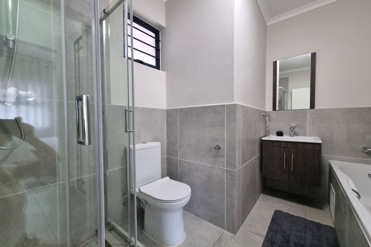 Modern bathroom featuring a glass shower enclosure, built-in bathtub, wall-mounted vanity with basin, and neutral grey tiling throughout.
