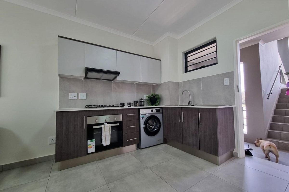 Modern kitchen featuring dark wood-look lower cabinets, light upper cabinets, built-in oven, gas hob, extractor fan, and tiled flooring with a neutral backsplash.