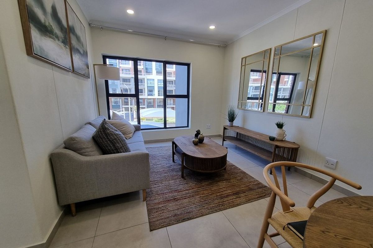A bright and modern living room featuring neutral tiled flooring, recessed downlighting, and a large window providing natural light.