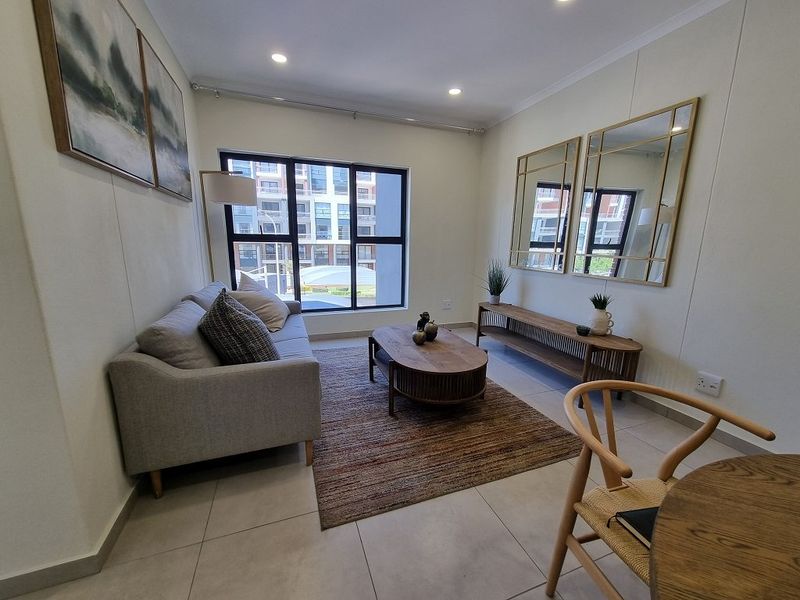 A bright and modern living room featuring neutral tiled flooring, recessed downlighting, and a large window providing natural light.