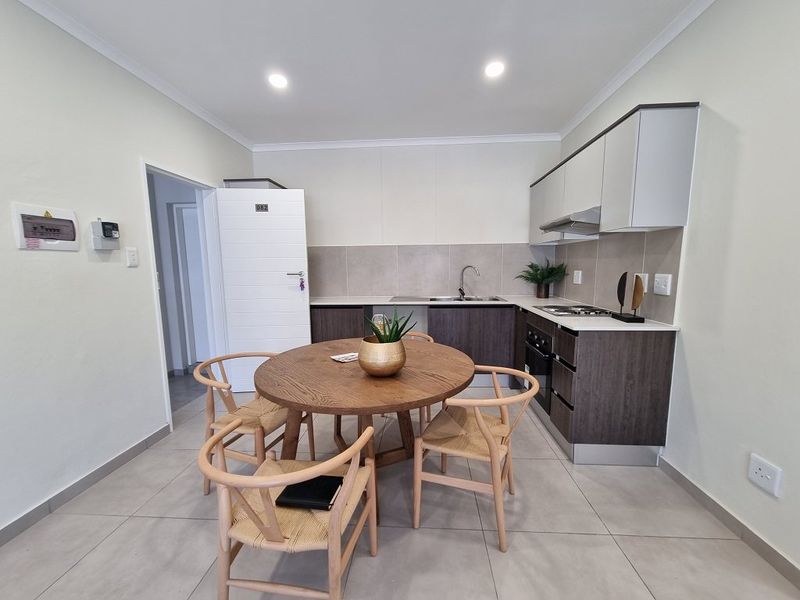 Modern open-plan kitchen featuring sleek cabinetry, integrated appliances, tiled backsplash, and neutral floor tiles, seamlessly flowing into the dining area.