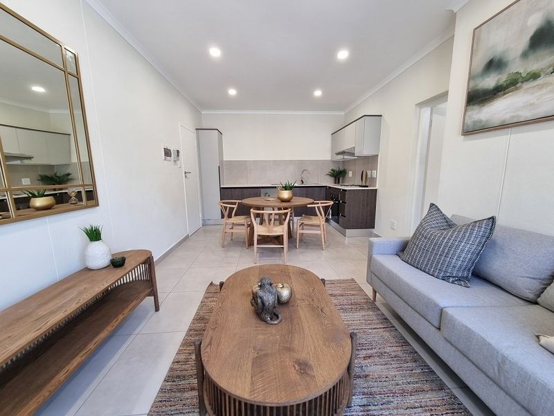 A modern open-plan living and kitchen area featuring tiled floors, recessed lighting, and contemporary cabinetry, creating a bright and functional living space.