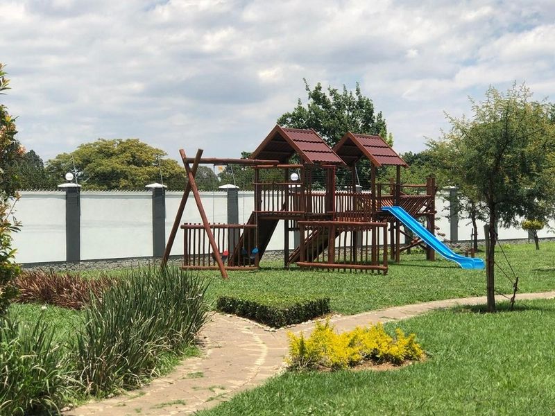 A well-maintained garden area featuring a paved pathway, manicured lawn, and a secure perimeter wall with electric fencing.