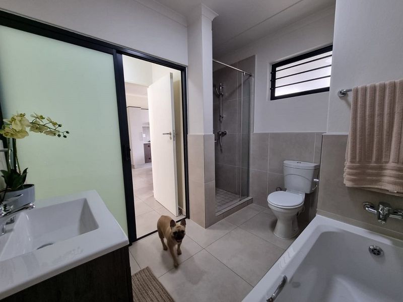 Modern bathroom featuring a glass-enclosed shower, bathtub, vanity with basin, and neutral floor-to-ceiling tiling.