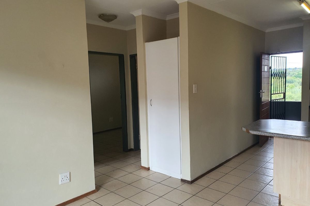 Open plan living area featuring tiled flooring, a built-in cupboard, and a breakfast counter, leading to an exterior entrance with a security gate.